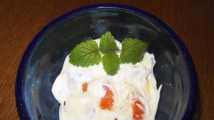 Eine Quarkspeise in einer Sch&uuml;ssel, garniert mit frischen Minzbl&auml;ttern, steht auf einem Holztisch.