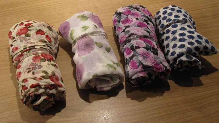 Vier ordentlich gerollte Halst&uuml;cher liegen auf einem hellen Holztisch, bereit zur Aufbewahrung oder zum Tragen.