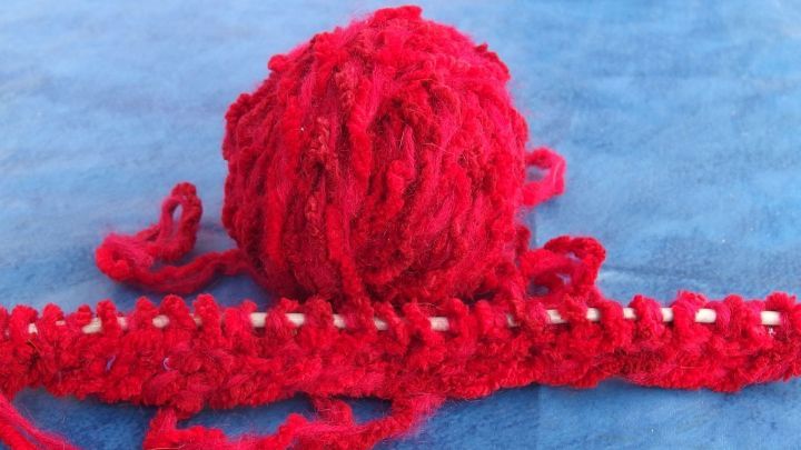 Ein rotes Wollkn&auml;uel liegt auf einer blauen Unterlage und wird verwendet, um eine Strickarbeit anzufertigen.