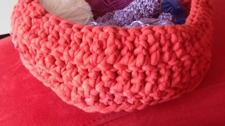 Ein roter Korb aus Jersey-Betttuch liegt auf einem Sofa und enth&auml;lt bunte Wollen und Kn&auml;uel in verschiedenen Farben.