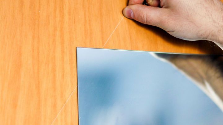 H&auml;nde entfernen einen aufgeklebten Spiegel von einer Holzschrankt&uuml;r in einem hellen Raum mit Holzstruktur.