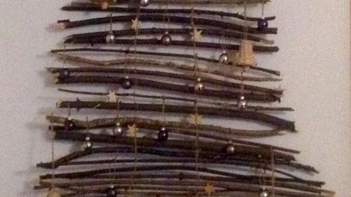 Ein Weihnachtsbaum aus &Auml;sten h&auml;ngt an einer Wand, geschm&uuml;ckt mit kleinen Glocken und einer Sternspitze.