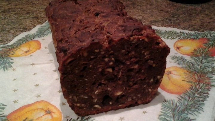 Ein dunkles Apfelbrot liegt auf einem dekorativen, weihnachtlichen Tischl&auml;ufer mit &Auml;pfeln und Tannenzweigen.