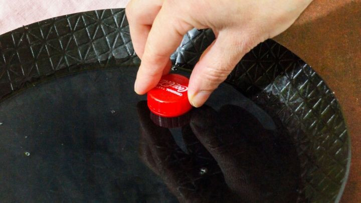 Eine Hand h&auml;lt einen roten Reinigungsknopf &uuml;ber einer angebrannten Pfanne, um sie effektiv zu reinigen.