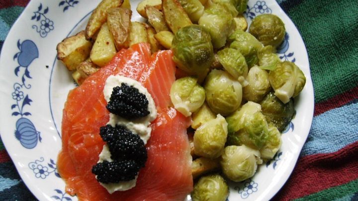 Auf dem Teller liegen knusprige Kartoffelspalten neben gebratenem Rosenkohl und Lachsforelle mit Kaviar.