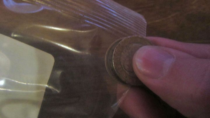 Ein Finger h&auml;lt eine M&uuml;nze, die in eine Plastikverpackung gedr&uuml;ckt wird, um sie ohne Schere zu &ouml;ffnen.