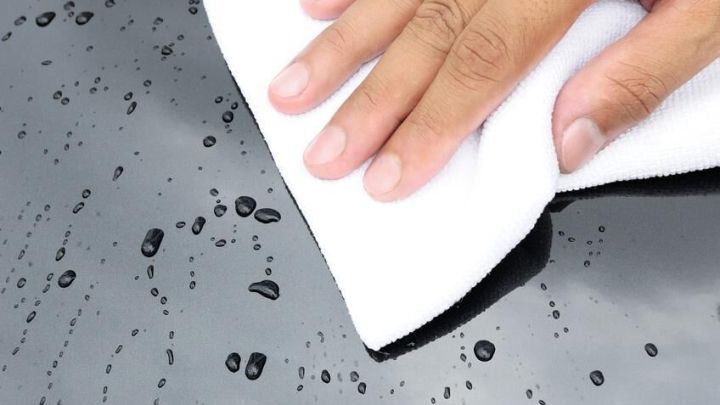 Eine Hand wischt mit einem wei&szlig;en Kaltwassertuch Wassertropfen von einer glatten Oberfl&auml;che, um streifenfrei zu reinigen.