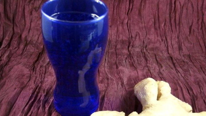 Ein blauer Trinkbecher steht auf einem roten Untergrund neben frischem Ingwer, der zur Linderung von Kopfschmerzen verwendet wird.