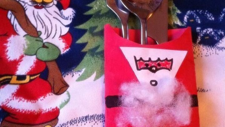 Ein Besteckhalter in Form von Nikolaus h&auml;lt Gabel, Messer und L&ouml;ffel und liegt auf einer festlichen Tischdecke.