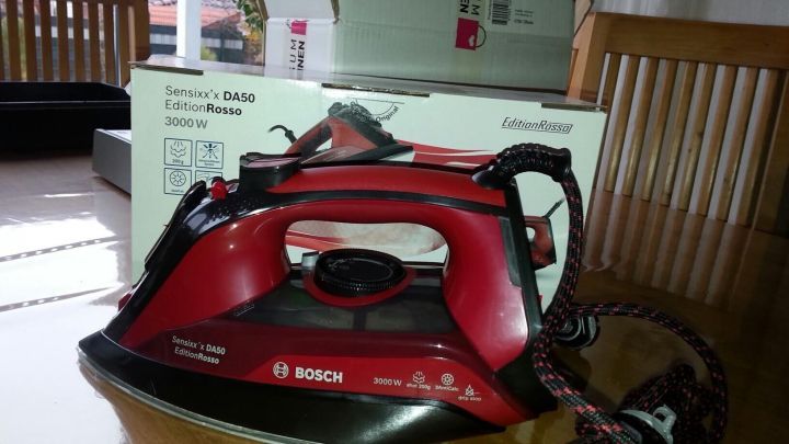 Ein rotes B&uuml;geleisen von Bosch steht auf einem Tisch, w&auml;hrend Verpackung im Hintergrund sichtbar ist.