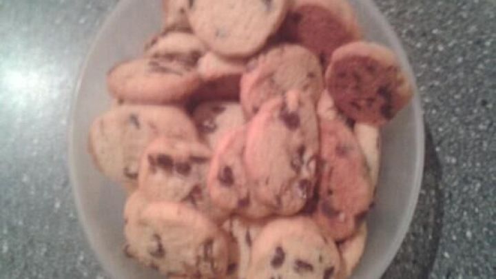 Eine Sch&uuml;ssel voller Schokotropfen-Pl&auml;tzchen liegt auf einem grauen Tisch und wartet darauf, genossen zu werden.