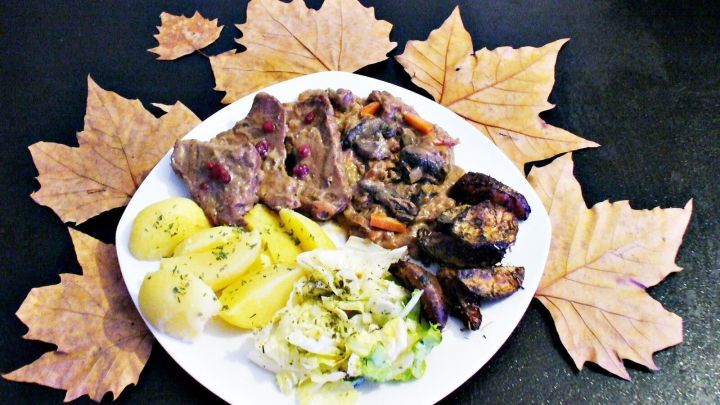 Ein Teller mit Gl&uuml;hwein-Steaktopf zeigt saftige Fleischst&uuml;cke, Kartoffeln und Salat, umgeben von herbstlichen Bl&auml;ttern.