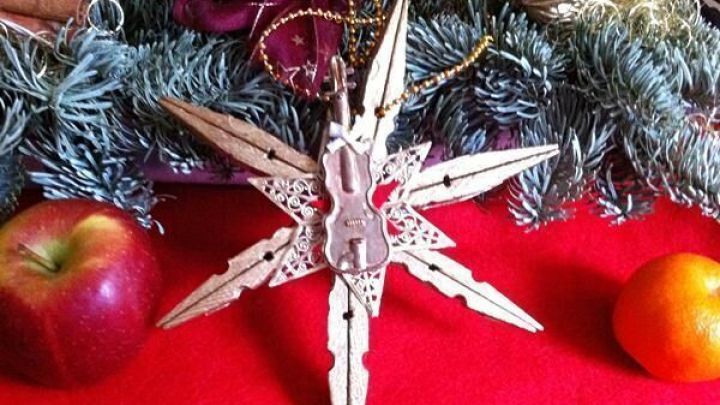 Ein Stern aus alten W&auml;scheklammern steht auf einem roten Tisch, umgeben von &Auml;pfeln und Tannenzweigen, festlich dekoriert.