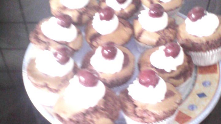 Schoko-Cupcakes mit Kirschen sind auf einem Teller angerichtet, garniert mit Sahne und Kirschen, vor einer dunklen K&uuml;chenfl&auml;che.