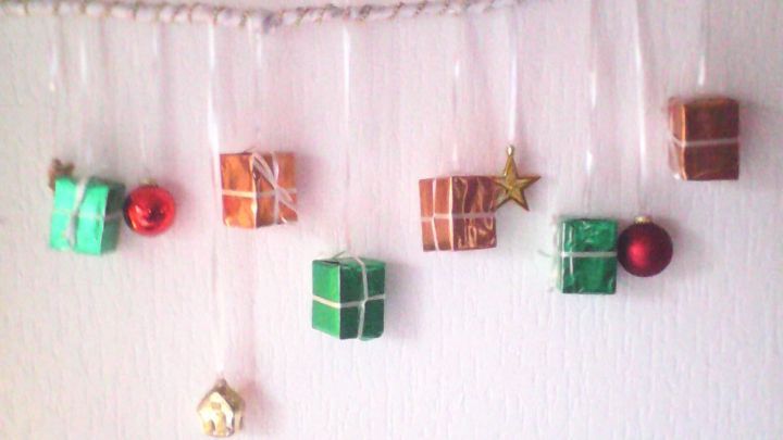 Geschenkboxen und Dekorationen h&auml;ngen an einem Weihnachtszweig an der Wand, festlich arrangiert im Wohnraum.