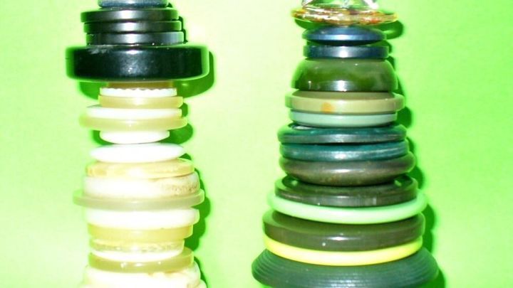 Zwei aus alten Kn&ouml;pfen gefertigte Anh&auml;nger in Form eines Schneemanns und eines Tannenbaums h&auml;ngen vor einem gr&uuml;nen Hintergrund.