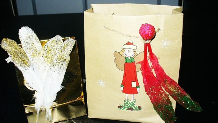 Funkelnde Engelsfedern liegen neben einem dekorativen Geschenkesack, der mit einem Engel und bunten Ornamenten verziert ist.