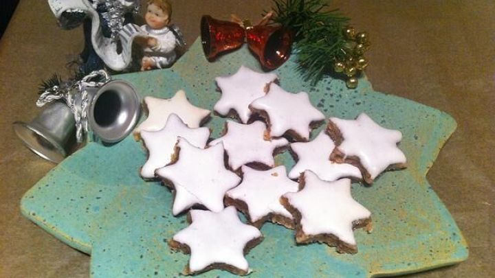 Zimtsterne liegen auf einem gr&uuml;nen Teller, umgeben von festlicher Dekoration, ideal f&uuml;r die Weihnachtszeit.