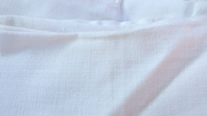 Wei&szlig;es Tuch liegt glatt auf einer Oberfl&auml;che, bereit f&uuml;r die W&auml;sche mit Waschn&uuml;ssen, Backpulver und Zitronen&ouml;l.