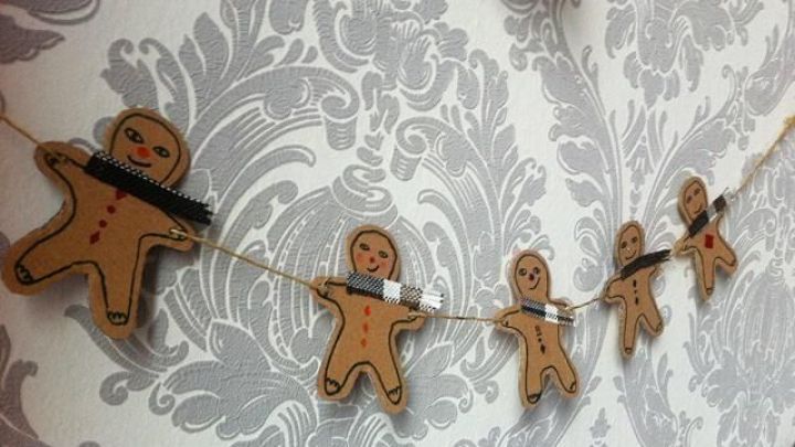 Eine Girlande aus Pappe zeigt Lebkuchenm&auml;nner, die an einer Schnur h&auml;ngen und vor einem eleganten, gemusterten Hintergrund schweben.