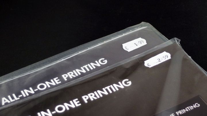 Zwei Verpackungen f&uuml;r All-in-One-Druckprodukte liegen auf einem schwarzen Hintergrund, die Preise sind sichtbar angebracht.