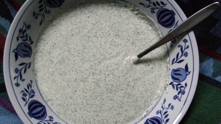 In einem bunten Tuch liegt eine Schale mit Gr&uuml;ne Sauce, verziert mit Blumenmotiven, in die ein L&ouml;ffel steckt.