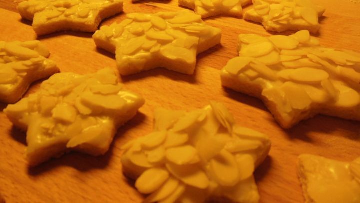 Sternf&ouml;rmige Butter-Mandel-Sterne liegen auf einem Holzbrett, dekoriert mit Mandelsplittern, in gem&uuml;tlicher K&uuml;chenszene.