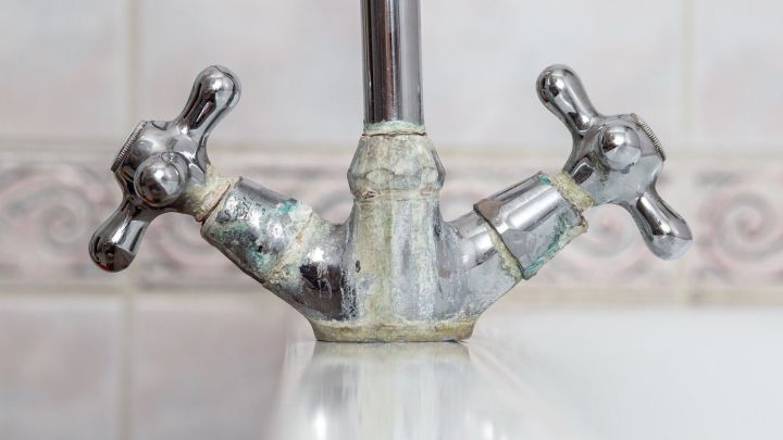 Ein verkalkter Wasserhahn zeigt Kalkablagerungen auf Chrom im Bad, umgeben von hellen Fliesen mit dezentem Muster.