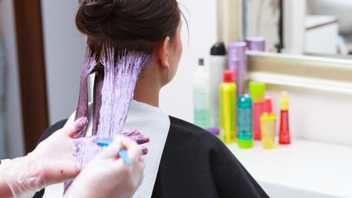 Eine Person mit gef&auml;rbten Haaren erh&auml;lt eine Behandlung zur Entf&auml;rbung, um die Haarfarbe zu ver&auml;ndern, umgeben von Pflegeprodukten.