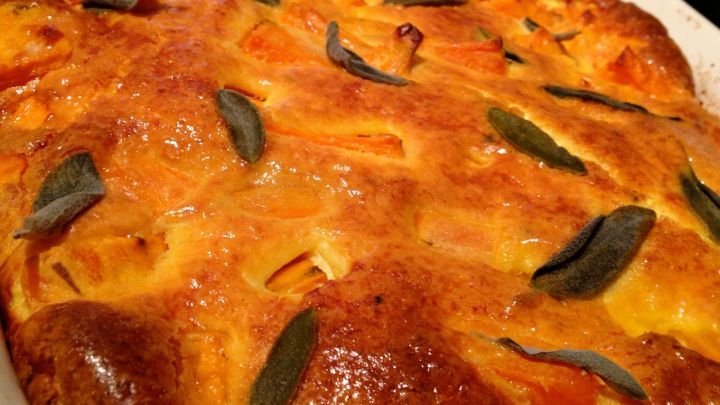 Ein gebr&auml;unter Eierauflauf mit S&uuml;&szlig;kartoffeln und frischen Salbeibl&auml;ttern ruht in einer wei&szlig;en Auflaufform.