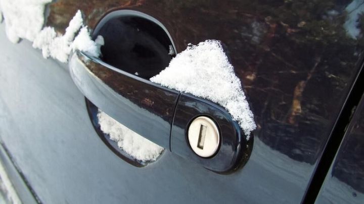 Ein schwarzes Auto mit einem eingefrorenen T&uuml;rschloss, umgeben von Schnee, ist bereit zum &Ouml;ffnen.