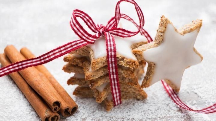 Zimtsterne, mit wei&szlig;er Glasur, sind stapelweise mit einem rot-wei&szlig;en Band gebunden. Daneben liegen Zimtstangen auf Mehl.