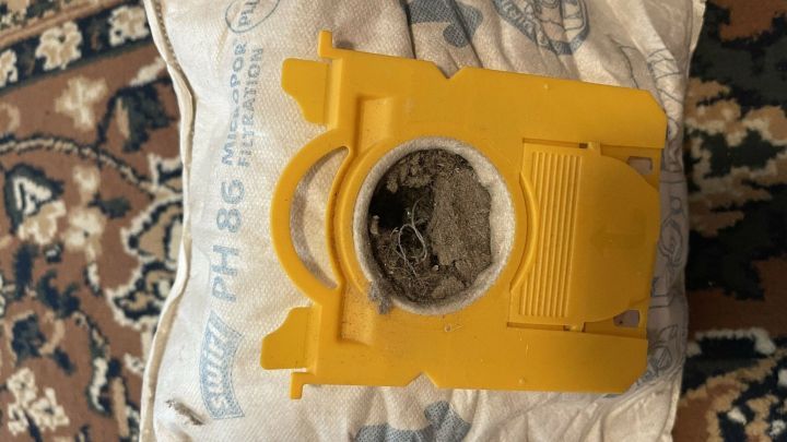 Eine gelbe Staubsaugert&uuml;te liegt auf einem Teppich, gef&uuml;llt mit Staub und Schmutz, bereit zur mehrmaligen Verwendung.