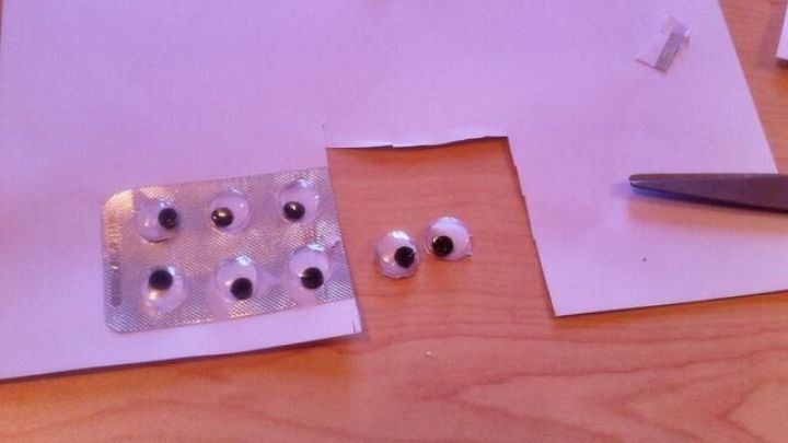 Wackelaugen liegen auf einem Tisch, w&auml;hrend jemand sie mit einer Schere bearbeitet, um sie herzustellen.