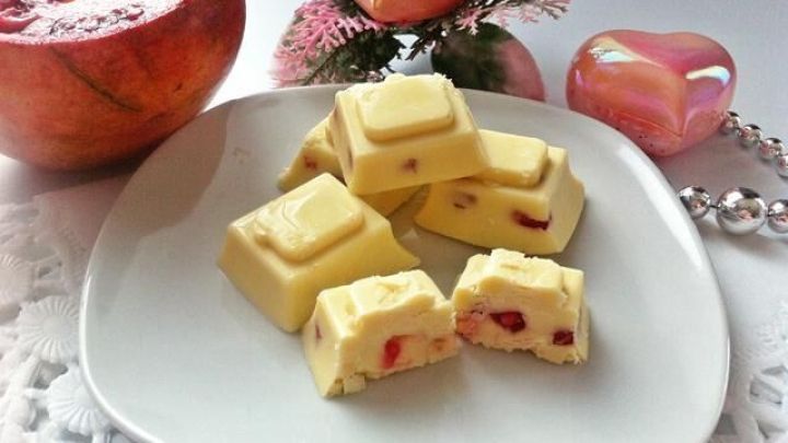 Auf einem Teller liegen Pralinen aus wei&szlig;er Schokolade, gef&uuml;llt mit Granatapfelkernen, umgeben von stilvollen Dekorationen.