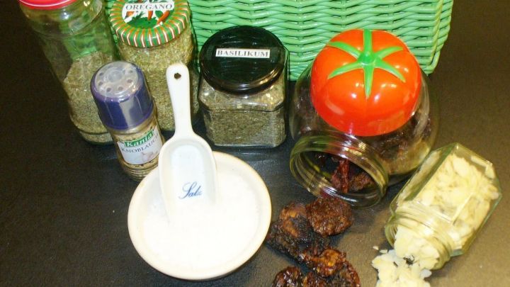 Verschiedene Kr&auml;uter- und Gew&uuml;rzgl&auml;ser, eine Sch&ouml;pfkelle und getrocknete Tomaten liegen bereit, um eine Pesto-W&uuml;rzmischung zu kreieren.