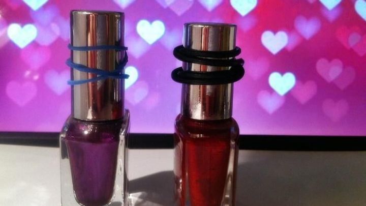 Zwei verklebte Nagellackflaschen stehen nebeneinander auf einem Tisch vor einem Hintergrund mit herzigen Motiven.