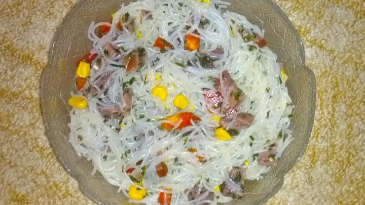 Ein Glasnudelsalat in einer Sch&uuml;ssel enth&auml;lt Mais und rote Paprika auf einem gemusterten Teppich. Text: "Glasnudel-Salat von &sbquo;Saxenmaedel&lsquo;".