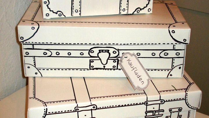 Drei shabby chic Kartons im Kofferlook stapeln sich dekorativ auf einer wei&szlig;en Oberfl&auml;che, umgeben von einem hellen Raum.