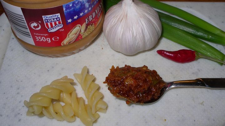 Eine Erdnussso&szlig;e wird zubereitet, um das "Sahnegulasch" zu erg&auml;nzen, umgeben von Zutaten wie Nudeln, Knoblauch und Chili.