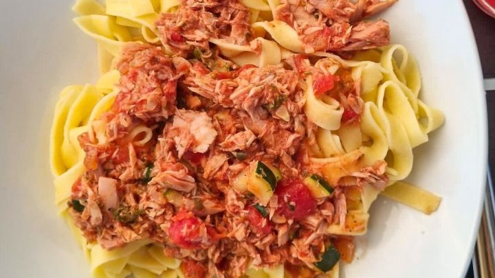 Ein Teller mit Pasta serviert, bedeckt mit Thunfisch-Bolognese, umgeben von einer eleganten Tischdecke und Besteck.