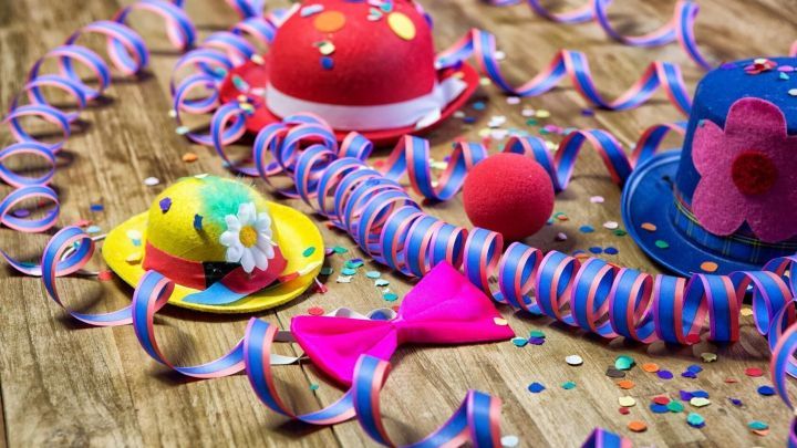 Bunte Faschingsklamotten und Konfetti liegen auf einem Holztisch, umgeben von spiralf&ouml;rmigen B&auml;ndern und Dekorationen.