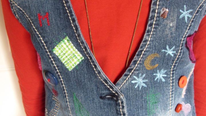 Eine bunte Jeansweste aus Resten wird getragen, verziert mit farbigen Patches und Kn&ouml;pfen, vor einem roten Oberteil.