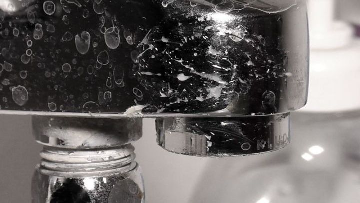 Ein Wasserhahn, der mit Essig gereinigt wird, zeigt Seifenblasen und R&uuml;ckst&auml;nde von Schmutz in einer modernen K&uuml;che.