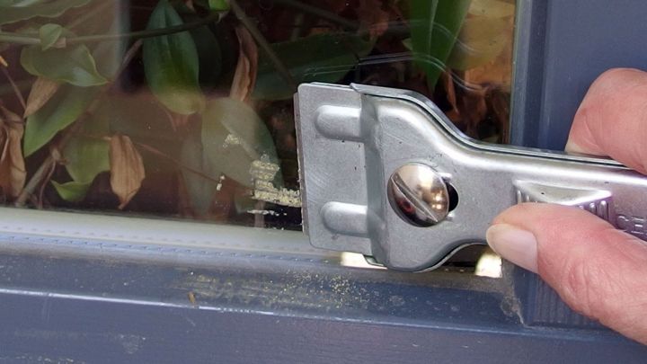 Ein Handwerker entfernt Klebereste von einer Fensterbank mit einer Rasierklinge, um die Oberfl&auml;che zu reinigen.