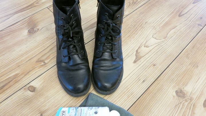 Schwarze Stiefel stehen auf einem Holzboden, w&auml;hrend Handcreme neben ihnen liegt, bereit zum Gl&auml;nzenbringen der Schuhe.