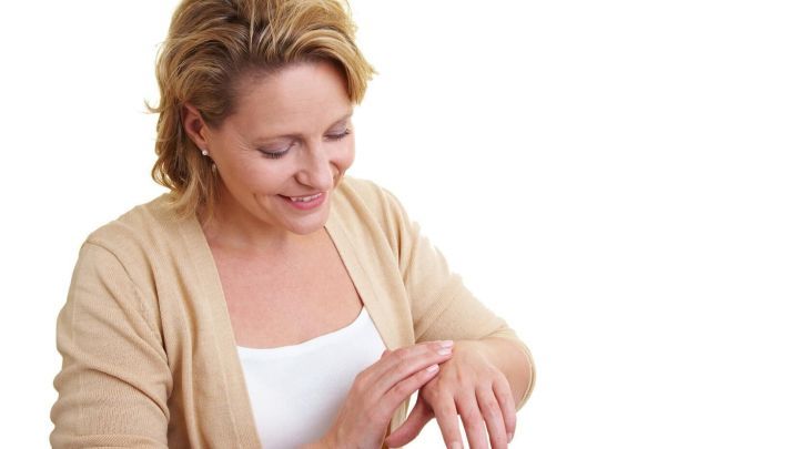 Eine Frau untersucht l&auml;chelnd ihr Handekzem, w&auml;hrend sie sanft mit einer Hand dar&uuml;ber streicht.