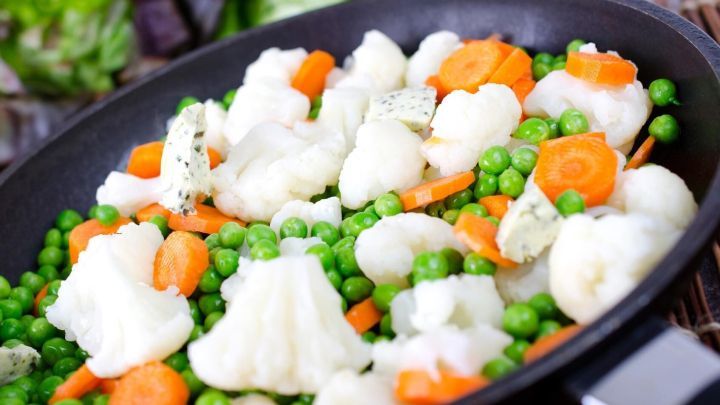 Bunte Gem&uuml;sebeilage mit Blumenkohl, Karotten und Erbsen wird in einer Pfanne frisch zubereitet, um ein leckeres Gericht zu verfeinern.
