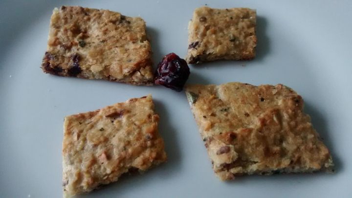 Zwei gesunde, zuckerfreie Kekse liegen auf einem wei&szlig;en Teller, umgeben von getrockneten Fr&uuml;chten.