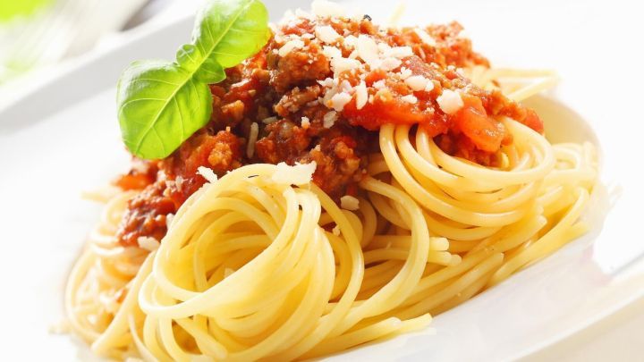 Spaghetti mit einer roten Chilisauce und einer Garnitur aus frischem Basilikum auf einem wei&szlig;en Teller, umgeben von gr&uuml;nem Licht.